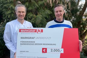 (Fotocredit: Werner Leister.) Von Bruder zu Bruder: Andreas Leister (im Bild rechts), übergibt die Spende im Namen der Bauunternehmung MARKGRAF an seinen Bruder Dr. Johannes Leister, der sie für die kleinen Patientinnen und Patienten in der KUNO Klinik St. Hedwig entgegen nimmt.