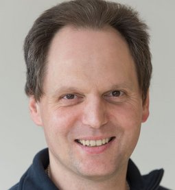 Herr Feifell hat etwas längere kurze braune Haare und eine halb Glatze